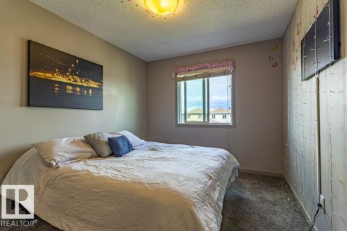 Carpeted bedroom featuring a large window, neutral wall paint, and a textured wall panel accent - 17123 49 Street, Edmonton, AB 