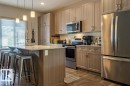 Modern kitchen featuring a breakfast bar island with seating, stainless steel appliances, wood-finish flooring, light-toned cabinetry, and pendant lighting - 17123 49 Street, Edmonton, AB 