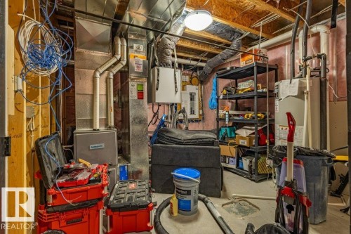 Utility room featuring exposed wooden joists, a water heater, furnace system, electrical panel, and exposed ductwork - 17123 49 Street, Edmonton, AB 