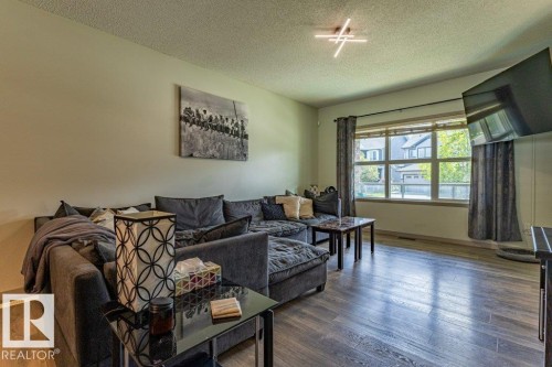Living area featuring wood-finish flooring, a large multi-pane window with blinds and drapes, and a contemporary ceiling light fixture - 17123 49 Street, Edmonton, AB 