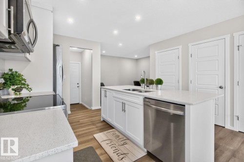 Modern kitchen island featuring a double-basin sink with a gooseneck faucet, integrated stainless steel dishwasher, white shaker-style cabinetry, and light-toned countertops - 1022 Hearthstone Boulevard, Sherwood Park, AB 