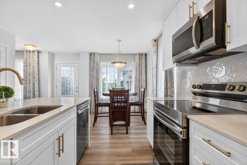 Bright kitchen featuring white cabinetry with gold-tone hardware, stainless steel appliances, and a hexagonal tile backsplash - 1022 Hearthstone Boulevard, Sherwood Park, AB 