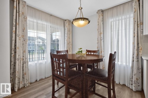 Dining space featuring wood-finish flooring, two large windows with sheer and patterned drapery, and a classic bowl pendant light fixture - 1022 Hearthstone Boulevard, Sherwood Park, AB 