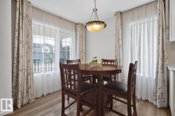 Dining space featuring wood-finish flooring, two large windows with sheer and patterned drapery, and a classic bowl pendant light fixture - 