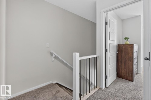 Upper-level landing featuring neutral carpeting, a contemporary white railing with black balusters, and a solid white door with recessed paneling - 1022 Hearthstone Boulevard, Sherwood Park, AB 