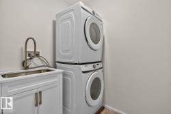 Dedicated laundry area featuring a stacked washer and dryer unit, a utility sink with a brushed bronze faucet, and white base cabinetry with matching hardware - 