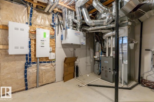 Utility space featuring exposed ductwork, two white electrical panels, a water heater, and a furnace - 1022 Hearthstone Boulevard, Sherwood Park, AB 