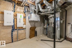 Utility space featuring exposed ductwork, two white electrical panels, a water heater, and a furnace - 