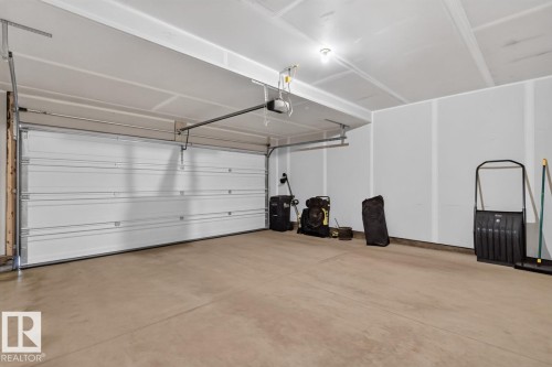 Spacious garage featuring a concrete floor, white panel garage door, and exposed ceiling joists - 1022 Hearthstone Boulevard, Sherwood Park, AB 
