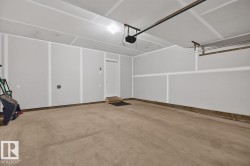 Spacious garage featuring a concrete floor, painted walls, overhead lighting, an automatic garage door opener, and a built-in storage rack - 