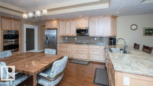 U-shaped kitchen with light wood cabinetry, stainless steel appliances, speckled countertops, and a tile backsplash - 58505 Rng Rd 260, Rural Westlock County, AB 
