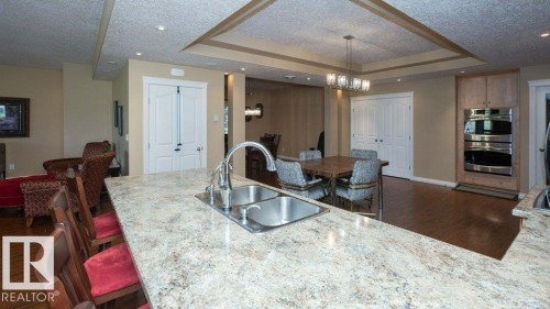 Spacious kitchen with a stone-finish countertop island featuring an undermount double-basin sink and a gooseneck faucet - 58505 Rng Rd 260, Rural Westlock County, AB 
