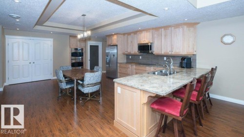Kitchen featuring wood-finish flooring, light wood cabinetry, stainless steel appliances, granite countertops, and a double basin sink - 58505 Rng Rd 260, Rural Westlock County, AB 