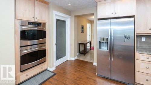Kitchen featuring wood-finish flooring, stainless steel double wall oven, stainless steel side-by-side refrigerator, light wood cabinetry, and a pantry door with frosted glass - 58505 Rng Rd 260, Rural Westlock County, AB 