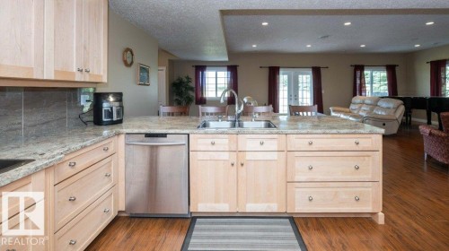 Kitchen island featuring a dual-basin stainless steel sink with a high-arc faucet, light-toned cabinetry, and a stone-finish countertop - 58505 Rng Rd 260, Rural Westlock County, AB 