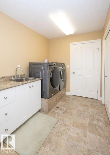 Laundry room featuring a utility sink with a high-arc faucet, white cabinetry with silver-tone hardware, and a stone-finish countertop - 58505 Rng Rd 260, Rural Westlock County, AB 