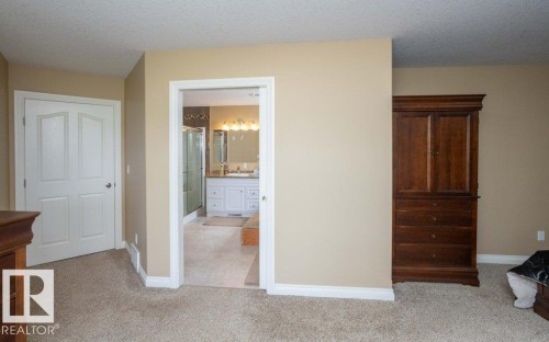 Plush carpeting in a neutral tone, featuring a doorway opening to a bathroom with dual vanities, a large mirror, and a glass-enclosed shower - 58505 Rng Rd 260, Rural Westlock County, AB 