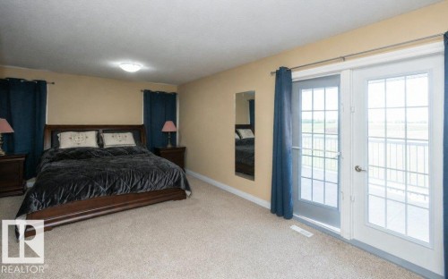 Carpeted bedroom featuring neutral wall tones, a ceiling-mounted light fixture, and double glass-paned doors opening to a balcony - 58505 Rng Rd 260, Rural Westlock County, AB 