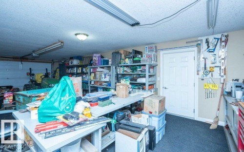 Garage interior featuring a white paneled door, gray carpeting, wall-mounted pegboard, overhead fluorescent lighting, and a white garage door - 58505 Rng Rd 260, Rural Westlock County, AB 