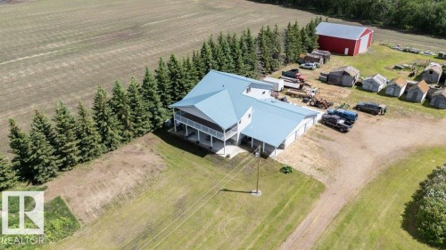 Expansive residential property featuring a primary residence with a metal roof, an upper-level screened porch, and an attached covered carport - 58505 Rng Rd 260, Rural Westlock County, AB 