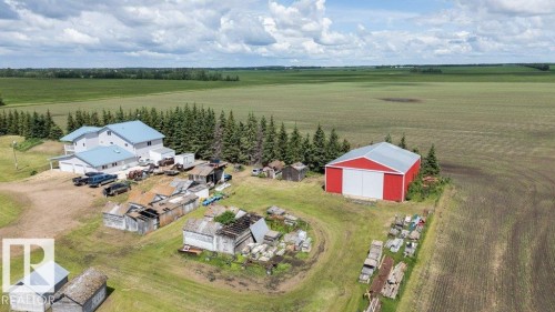 Expansive property featuring a multi-level residence with a light blue roof, a large red barn with white doors, multiple outbuildings, and surrounding agricultural fields - 58505 Rng Rd 260, Rural Westlock County, AB 