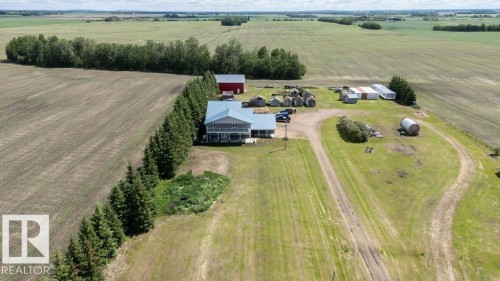 Expansive rural property featuring a two-story residence with a wraparound porch and light-colored siding, a red barn, and multiple outbuildings - 58505 Rng Rd 260, Rural Westlock County, AB 
