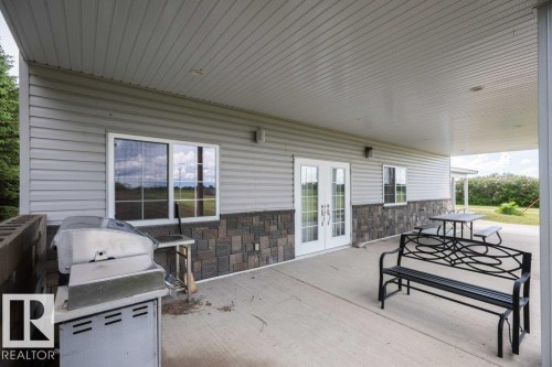 Expansive covered patio featuring a concrete surface, light gray siding, and stone veneer accents - 58505 Rng Rd 260, Rural Westlock County, AB 