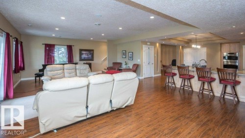 Open-concept living space featuring wood-finish flooring, recessed lighting, a breakfast bar with built-in cabinetry, double wall ovens, and a double basin sink - 58505 Rng Rd 260, Rural Westlock County, AB 