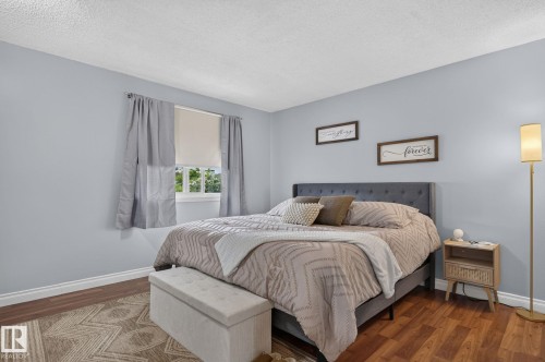 Bedroom featuring a window with roller shade and curtains, light blue walls, and wood-finish flooring - 14612 29 Street Nw, Edmonton, AB 