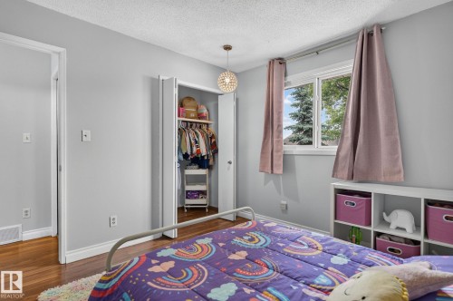 Bedroom featuring wood-finish flooring, a double-door closet, and a single window with white trim - 14612 29 Street Nw, Edmonton, AB 