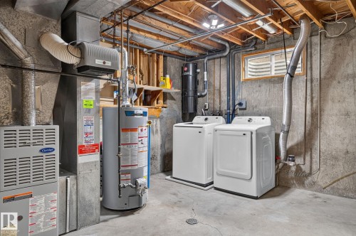 Utility area featuring a washer and dryer, water heater, furnace, and exposed ceiling joists - 14612 29 Street Nw, Edmonton, AB 