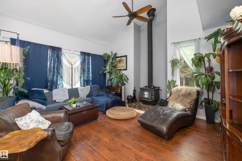 Living area featuring wood-finish flooring, a wood-burning stove with a stone hearth, a ceiling fan, and high vaulted ceilings - 7 53424 Range Road 13, Rural Parkland County, AB 