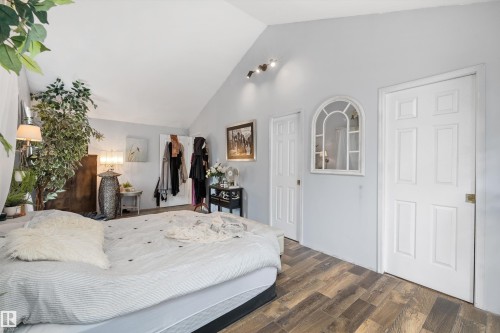 Vaulted ceiling bedroom featuring wood-finish flooring, white paneled doors, and a decorative arched window - 7 53424 Range Road 13, Rural Parkland County, AB 