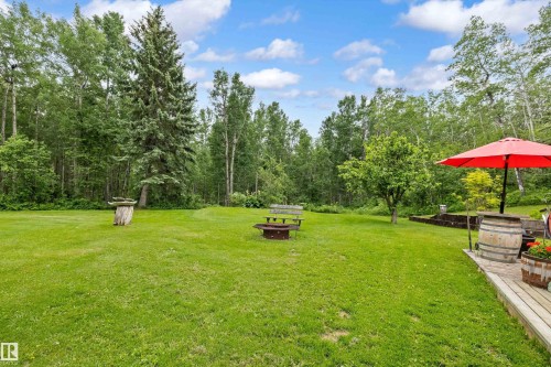 Expansive green lawn surrounded by mature trees, featuring a wooden deck with a built-in planter - 7 53424 Range Road 13, Rural Parkland County, AB 