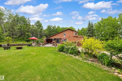 Spacious yard featuring a large patio, lush green lawn, mature trees, and established garden beds - 7 53424 Range Road 13, Rural Parkland County, AB 