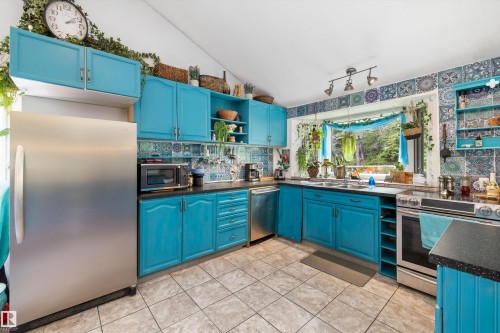 Kitchen featuring vibrant blue cabinetry, tile flooring, stainless steel appliances, a tile backsplash, and track lighting - 7 53424 Range Road 13, Rural Parkland County, AB 
