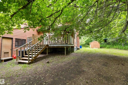 Rear exterior featuring a wooden deck with railing and stairs, siding in a natural hue, and a detached storage shed on a partially grassed lot - 7 53424 Range Road 13, Rural Parkland County, AB 