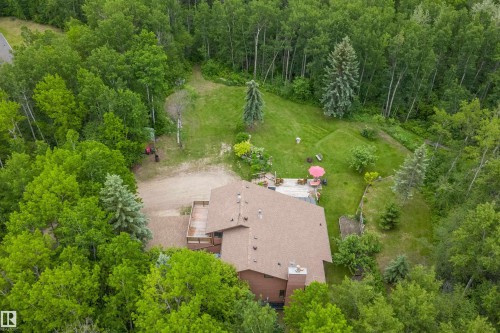 Expansive property surrounded by mature trees, featuring a multi-level deck, a sloped grassy area, and a gravel driveway - 7 53424 Range Road 13, Rural Parkland County, AB 