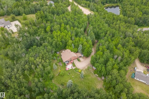 Expansive treed parcel featuring a primary residence with a red hip roof, a surrounding green lawn, and a natural pond - 7 53424 Range Road 13, Rural Parkland County, AB 