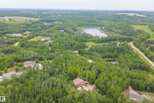 Expansive rural landscape featuring a private residence with surrounding mature trees, a private pond, and a nearby larger body of water - 7 53424 Range Road 13, Rural Parkland County, AB 
