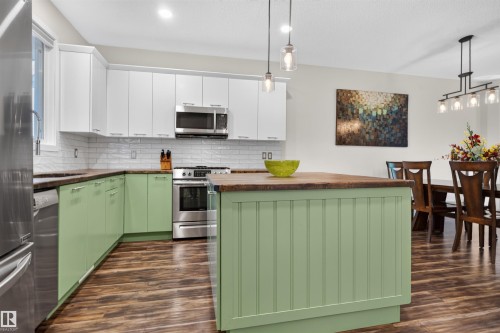 Kitchen featuring wood-finish flooring, two-tone cabinetry, stainless steel appliances, a subway tile backsplash, and an island with a wood countertop - 6928 22 Avenue, Edmonton, AB 