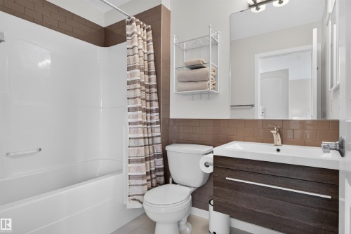 Bathroom featuring a white bathtub and shower surround, a white toilet, and a vanity with wood-finish cabinetry - 6928 22 Avenue, Edmonton, AB 