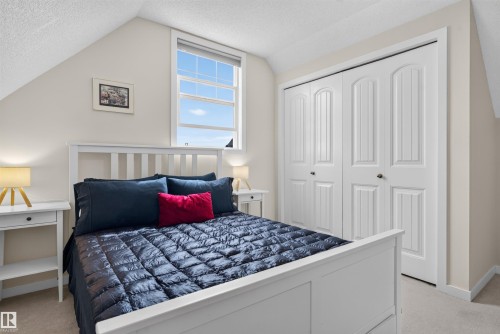 Bright bedroom featuring architectural sloped ceilings, a double window with blinds, and white bi-fold closet doors with decorative paneling - 6928 22 Avenue, Edmonton, AB 