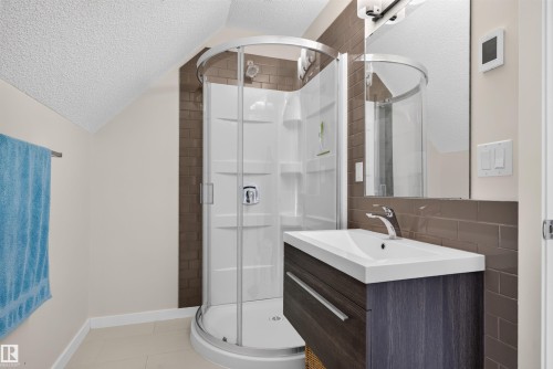 Contemporary bathroom featuring a corner shower with curved glass enclosure and a dark wood-finish vanity with an integrated white sink - 6928 22 Avenue, Edmonton, AB 