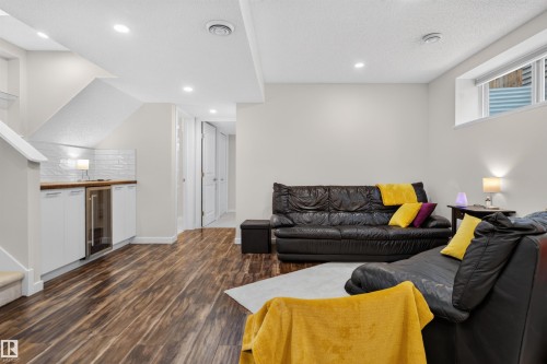 Lower-level living area featuring wood-finish flooring, recessed lighting, and a built-in wet bar with a beverage refrigerator and subway tile backsplash - 6928 22 Avenue, Edmonton, AB 