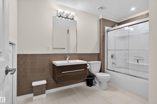 Contemporary bathroom featuring a floating wood-finish vanity with an integrated sink, a full-width mirror, and a three-light vanity fixture - 6928 22 Avenue, Edmonton, AB 