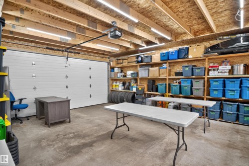 Spacious garage featuring a concrete floor, exposed wood beam ceiling, ample built-in shelving, and strip lighting - 6928 22 Avenue, Edmonton, AB 
