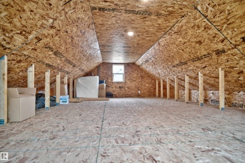 Unfinished attic space featuring oriented strand board walls and flooring, exposed structural supports, and a single window - 6928 22 Avenue, Edmonton, AB 