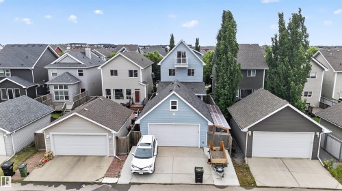 Light blue detached home featuring a two-car garage, upper-level balcony, and mature trees - 6928 22 Avenue, Edmonton, AB 