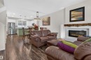 Living area featuring wood-finish flooring, a contemporary electric fireplace with a white tile surround, and a rustic wood mantel - 6928 22 Avenue, Edmonton, AB 